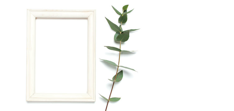 White wooden photo frame and green eucalyptus leaves on white background. Flat lay top view copy space. Stylish minimal composition, artwork mockup, picture frame, home decoration