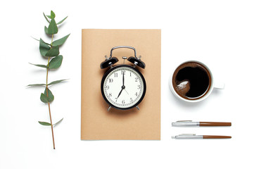 Flat lay cup of black coffee, black alarm clock, notebook, diary, eucalyptus on white background top view copy space. Minimalistic food concept, Feminine desk workspace, time to work coffee background