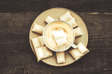 A cup of coffee with white porous chocolate on a wooden background. Top view