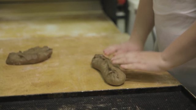 Close up for baker hands preparing raw rye for the loaf, food concept. Woman hands making a baguette from the raw rye dough onwooden board at the bakery.