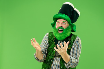 A smiling surprised happy senior man in a leprechaun hat with beard at green studio. He celebrates...