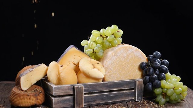 Set of hard cheese beautifully put in wooden box decorated with grapes. Spices falling down on composition in slow motion. Restaurant showroom. Food art. hd