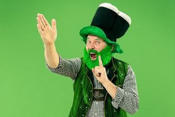 A smiling surprised happy senior man in a leprechaun hat with beard at green studio. He celebrates...