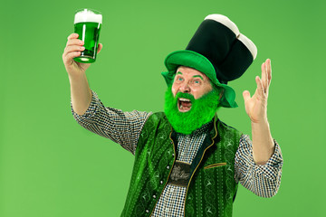 A smiling happy senior man in a leprechaun hat with green beer at studio. He celebrates St....