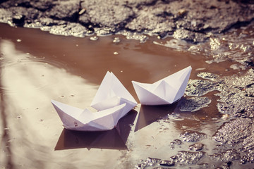 Fototapeta na wymiar The paper boat floats through the spring puddles. Children's entertainment.