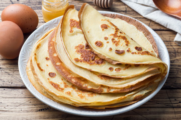 Thin pancakes on a plate. Wooden background. Ingredients to cooking eggs, milk, flour.
