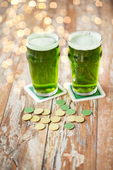 st patricks day, holidays and celebration concept - glasses of green beer and gold coins on wooden table