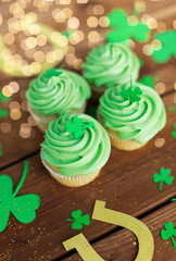 st patricks day, holidays and cooking concept - green cupcakes, horseshoes and shamrock on wooden table
