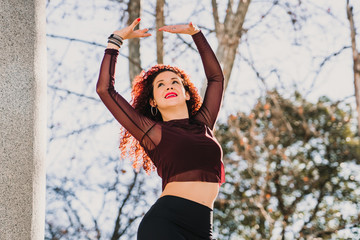 Fototapeta na wymiar .Young and attractive red haired latin woman dancing urban style on the street on a sunny winter day. Wear sports clothes Positive attitude, happiness. Lifestyle.