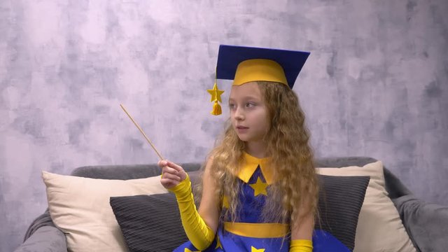 Magic astronomer in academic cap with magic wand showing on something in empty copyspace. Stargazer girl doing witchcraft with magic stick. Astronomer predicts future by stars