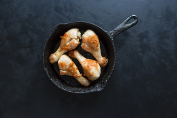 Fried chicken legs on a black background in an old pan.