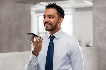 business, communication and technology concept - smiling indian businessman using voice command...
