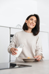 Image of beautiful woman 30s making breakfast with oatmeal and fruits, while standing in modern kitchen at home
