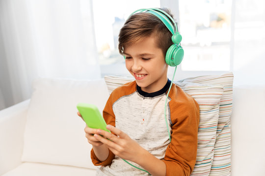 children, technology and people concept - happy smiling boy with smartphone and headphones listening to music at home