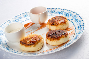 Curd pancakes with sour cream and jam on a white plate. Traditional Ukrainian and Russian dessert.