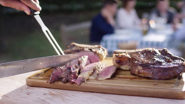 Steak is cut into strips on a wooden plate at a family celebration. - Steak wird auf einer Familienfeier auf Holzplatte in Streifen geschnitten. 4k PRORES Footage