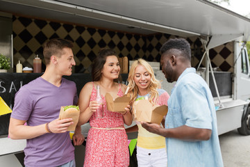 leisure and people concept - happy friends with drinks eating and talking at food truck