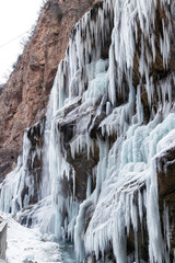 Fototapeta na wymiar Large frozen icicles on site of waterfalls in mountainous area