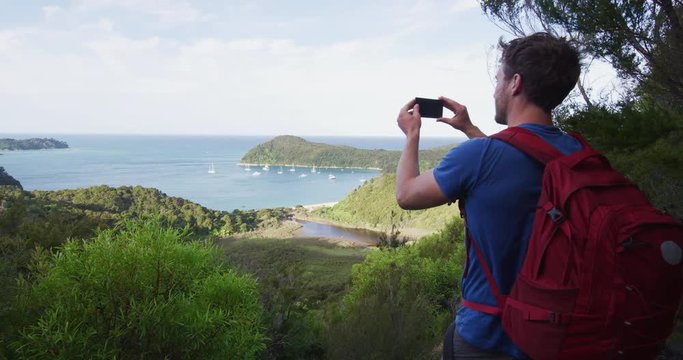 New Zealand travel man taking pictures with smart phone of the Anchorage in Abel Tasman National park, New Zealand vacation. Male backpacker tramping hiking on Abel Tasman Coast Track. SLOW MOTION.