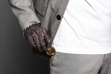 cropped shot of tattooed man in suit putting bitcoin in pocket isolated on grey