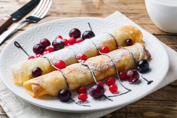 Pancakes tube with chocolate and berries on a plate. Wooden background.