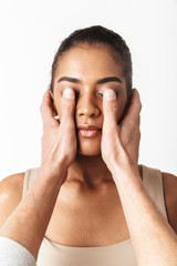 African woman posing isolated over white wall background while someone's hands covering her eyes.