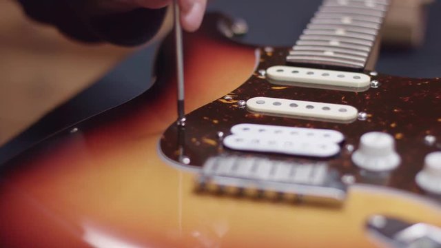 Man repairing a guitar, tightens the screw