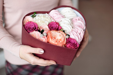 A bouquet of flowers and marshmallows in a gift box of heart in female hands.Congratulatory concept, sale.Close-up.