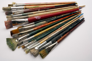 A collection of well used art paint brushes on white paper surface