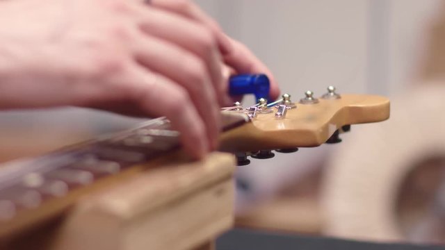 Man tunes guitar strings with peg winder
