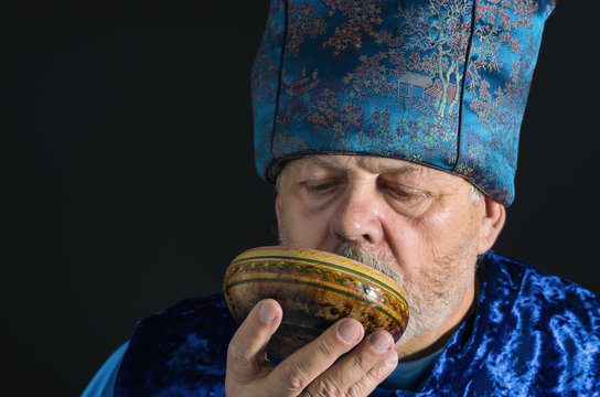 Nice portrait of bearded senior man in blue oriental clothes drinking tea from piola