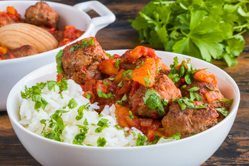 Moroccan meatballs in a spicy sauce with tomatoes and dried apricots and boiled rice. White casserole and bowl on wooden rustic table