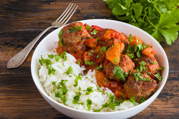 Moroccan meatballs in a spicy sauce with tomatoes and dried apricots and boiled rice in white bowl on wooden rustic table