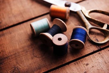 Old sewing thread wooden reels or bobbins and a gold scissors on a old rustic work bench. Intentionally shot in muted retro-vintage tone and shallow depth of field. (soft focus)