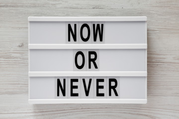 'Now or never' word on modern board on a white wooden surface, top view. From above, flat lay, overhead.