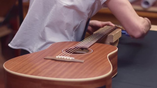 Luthier tune guitar strings with peg winder, slow motion