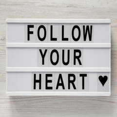 Lightbox with text 'Follow your heart' on a white wooden background, top view. Flat lay, overhead. Valentine's Day 14 February.