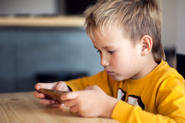 Children, technology and internet concept. Little smiling boy playing games on digital smartphone