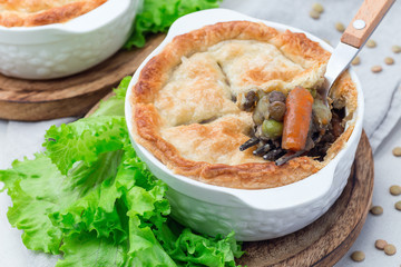 Vegetarian pot pie with lentil, mushroom, potato, carrot and green peas, covered with puff pastry, in baking dish, horizontal