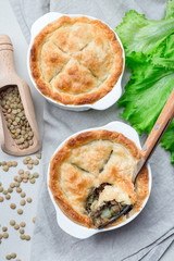 Vegetarian pot pie with lentil, mushroom, potato, carrot and green peas, covered with puff pastry, in a baking dish, vertical, top view