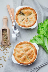 Vegetarian pot pie with lentil, mushrooms, potato, carrot and green peas, covered with puff pastry, in baking dish, vertical, top view