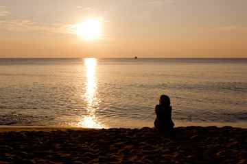 Fototapeta premium silhouette of a woman sitting on a beach at sunset