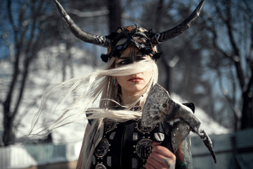 Portrait of beautiful warrior woman in image of viking with horned helmet and ax.