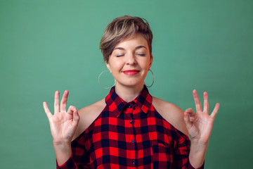 People,emotions and yoga concept -a portrait of woman relaxing and smiling with eyes closed doing meditation gesture with fingers.