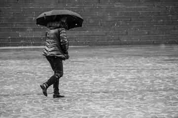  Portrait of woman walking with umbrella and winter coat by snowy day on cobbles place