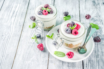 Recipe ideas for summer diet breakfast, healthy morning dessert Cheesecake in portioned jars with summer berries - raspberry, blueberry, blackberry. On wooden background copy space