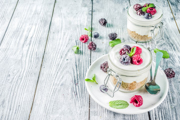 Recipe ideas for summer diet breakfast, healthy morning dessert Cheesecake in portioned jars with summer berries - raspberry, blueberry, blackberry. On wooden background copy space