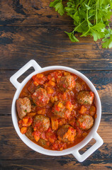 Moroccan meatballs in a spicy sauce with tomatoes and dried apricots. White casserole on wooden rustic table, top view