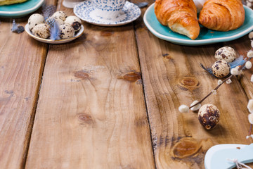 Easter breakfast flat lay with fresh coffee, berries and pastries , orange tulips, croissants with bacon and various sweets , colored quail eggs and spring holidays decorations. Top view. Copy space.