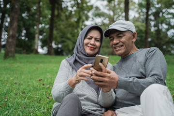 senior muslim couple using smartphone together in the park